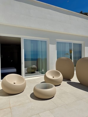 A modern outdoor seating area with round, beige chairs and a glass door leading to a room.