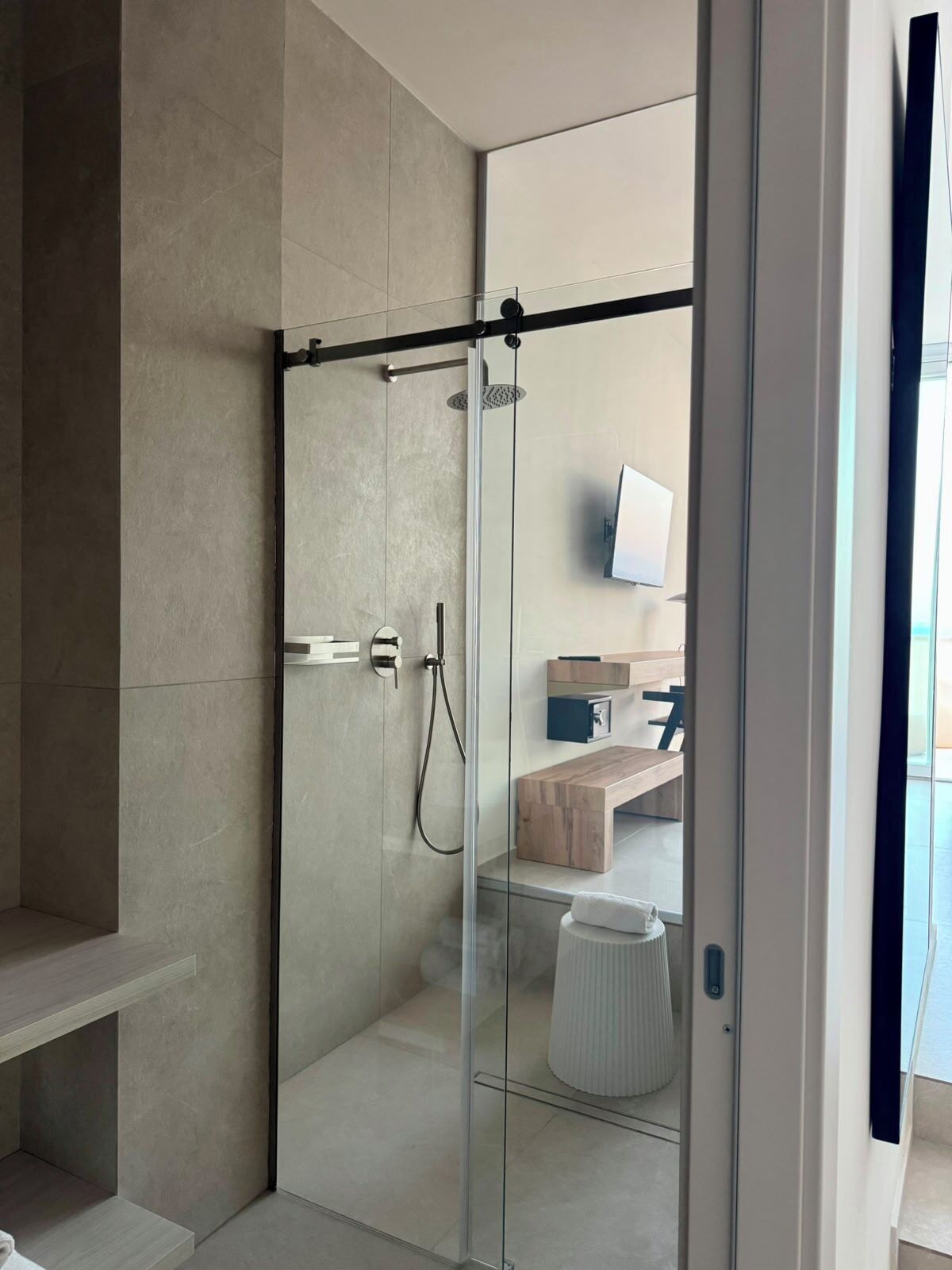 A modern bathroom with a glass shower enclosure, a wooden vanity, and a mounted television.