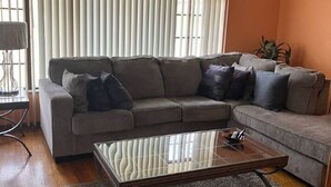 A living room with a sectional sofa, a glass coffee table, and a lamp.