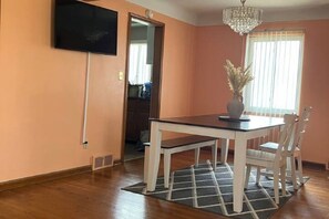 A dining area with a wooden table, white chairs, a chandelier, and a vase with dried plants. - Oak Park Beauty (Oak Park)