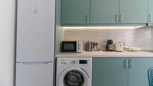 Eine kompakte Küche mit Kühlschrank, Mikrowelle, Wasserkocher, Toaster und Waschmaschine.