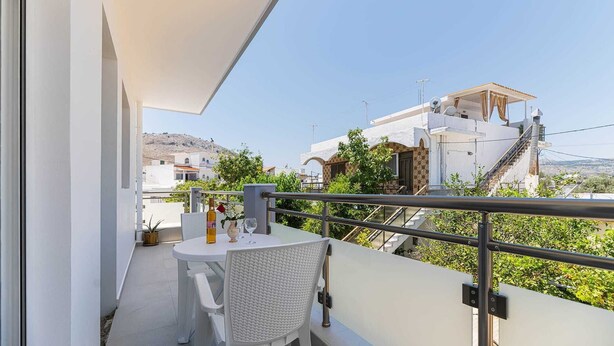 Ein Balkon mit Tisch und Stühlen, einem Blumentopf und Blick auf Gebäude im Hintergrund.