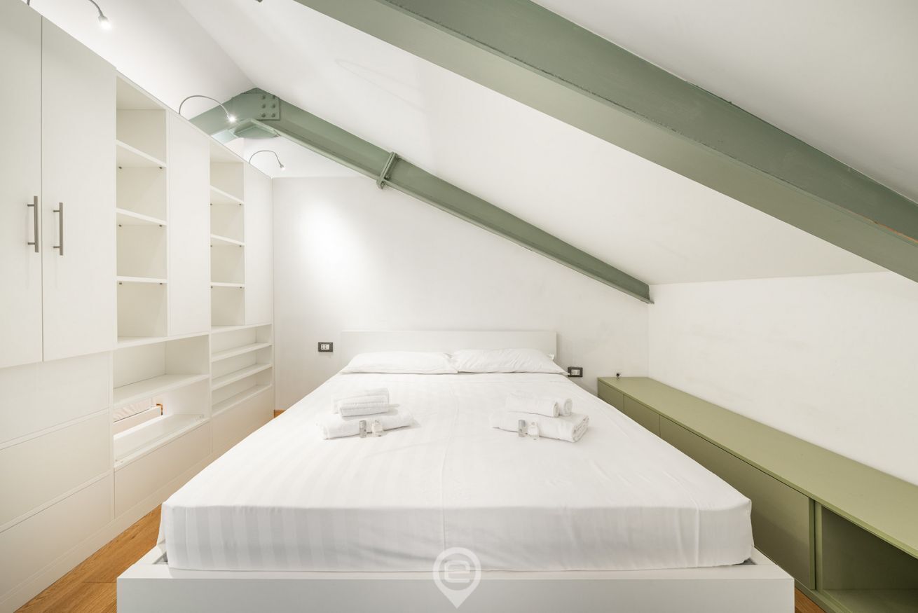 A modern bedroom with a large bed, built-in wardrobe, and a green accent wall.