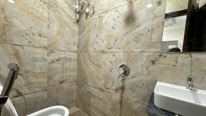 Une salle de bain avec un mur en marbre, un lavabo sur pied blanc et une douchette à main.