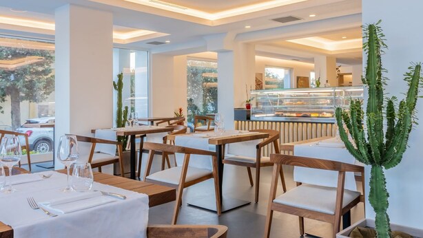 Un restaurant avec des tables et des chaises en bois, un cactus et un présentoir de desserts.