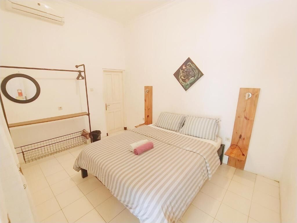 A bedroom with a bed, a wooden headboard, a wall-mounted mirror, and a door.