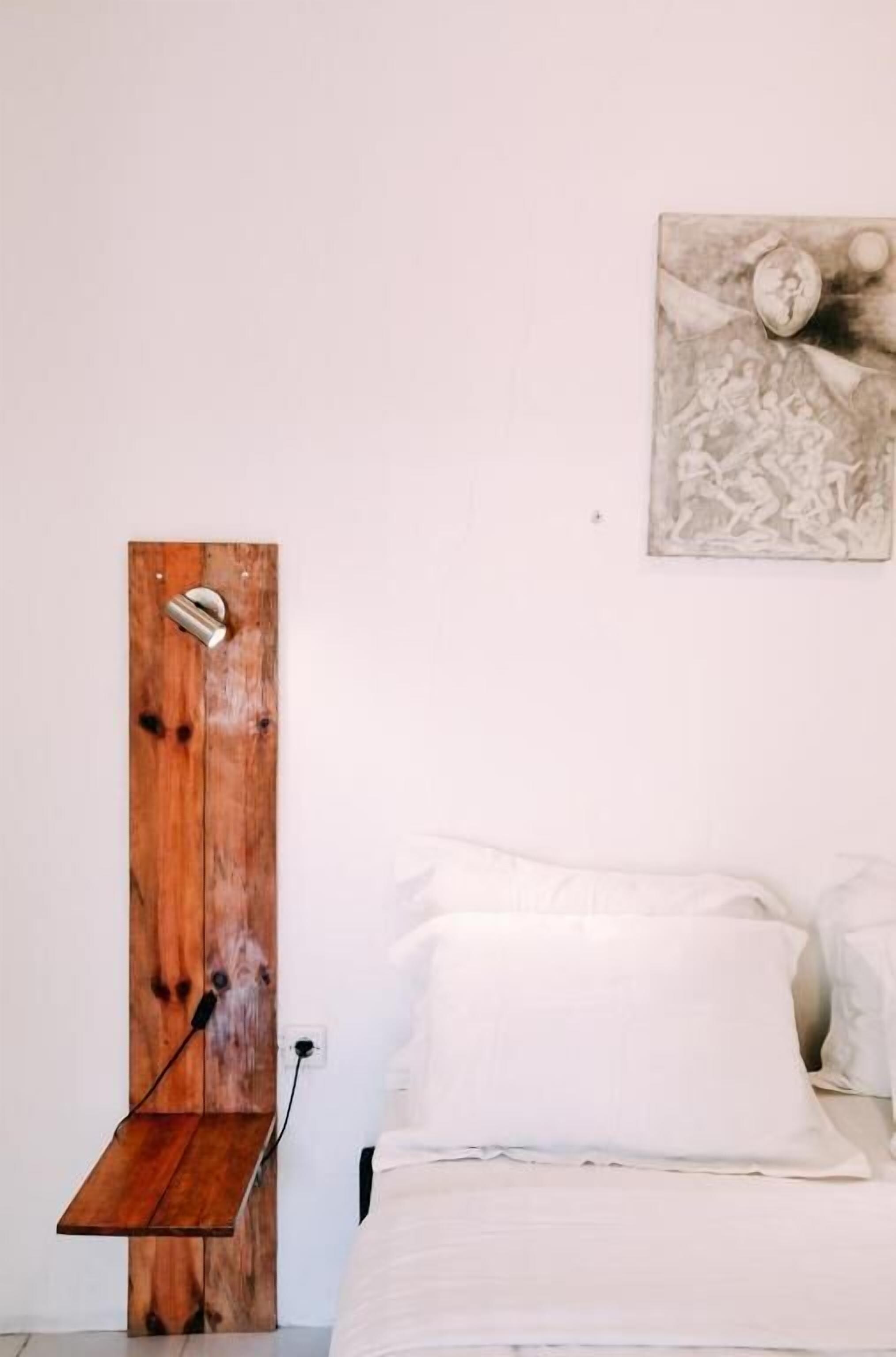 Une chambre avec une porte en bois, une poignée en métal, un lit blanc avec des oreillers et une œuvre d’art accrochée au mur.