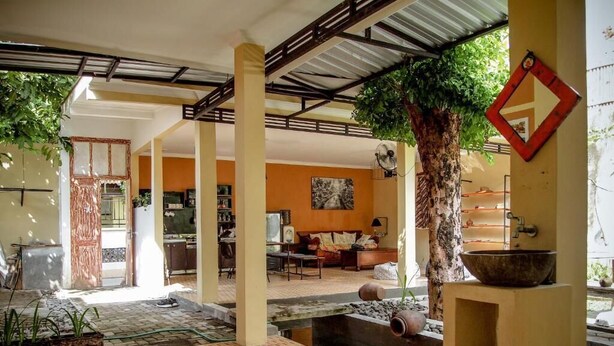 A spacious indoor area with a central water feature, a seating area with a sofa and chairs, and a large tree providing shade. - Pojok Pas Guesthouse (Yogyakarta)