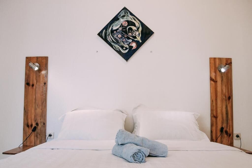 Una cama con sábanas blancas, dos cabeceros de madera y un cuadro en la pared superior.