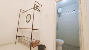 A bathroom with a toilet, a shower area, and a metal rack with a towel. - Pojok Pas Guesthouse (Yogyakarta)