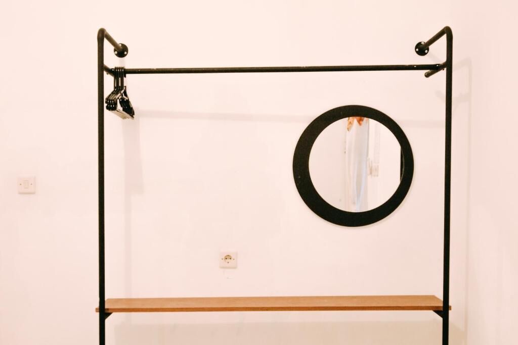A minimalist room with a black metal frame structure, a circular mirror, and a wooden shelf.