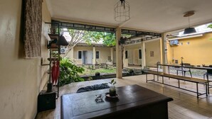 An open-plan living area with a wooden table, benches, and a view of a courtyard. - Pojok Pas Guesthouse (Yogyakarta)