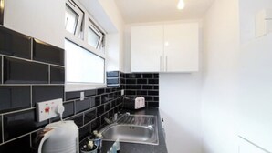 A compact kitchen with black and white tiles, a built-in sink, and a toaster. - Coventry Road Studio Flat (Southampton)