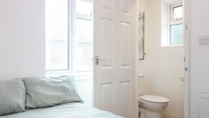 A bedroom with a bed, a white door, a window, and a toilet. - Coventry Road Studio Flat (Southampton)