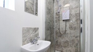 A bathroom with a white sink, a shower with a glass door, and marble tiles. - Coventry Road Studio Flat (Southampton)