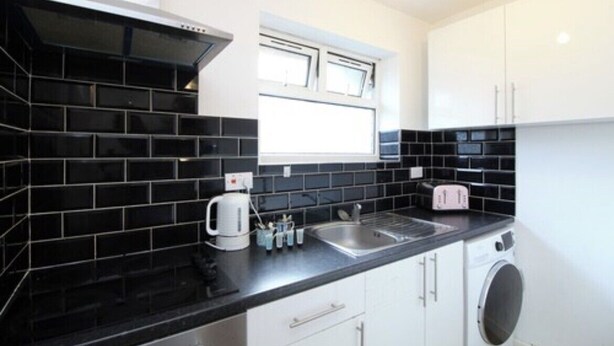 A compact kitchen with black and white tiles, a built-in oven, a window, and a washing machine. - Coventry Road Studio Flat (Southampton)
