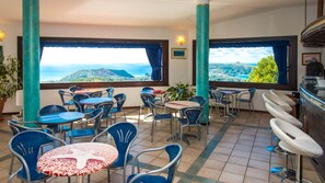 Een terras met tafels en stoelen, uitzicht op zee en een bar.