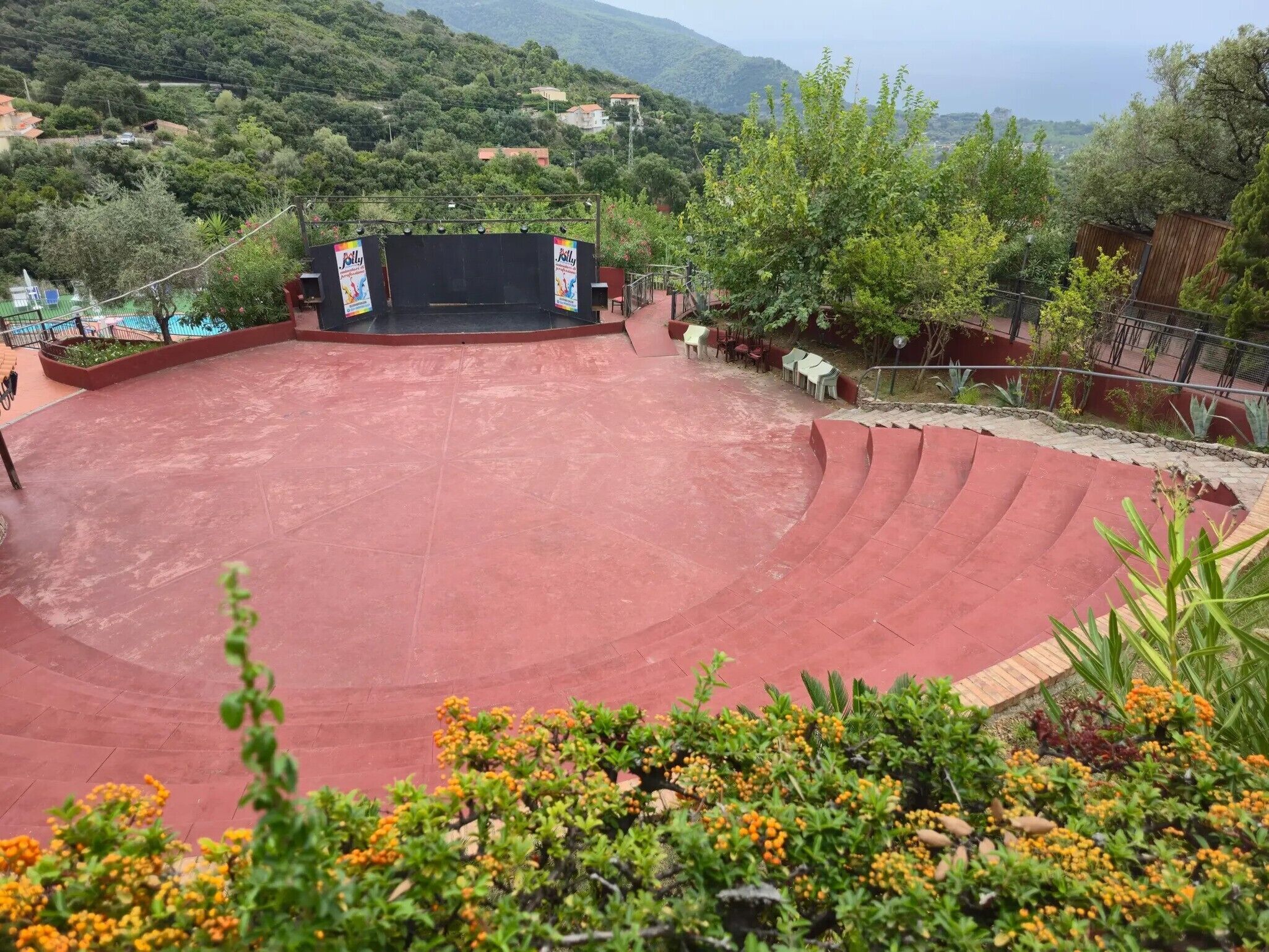 An outdoor amphitheater with tiered seating, surrounded by greenery and overlooking a hilly landscape.