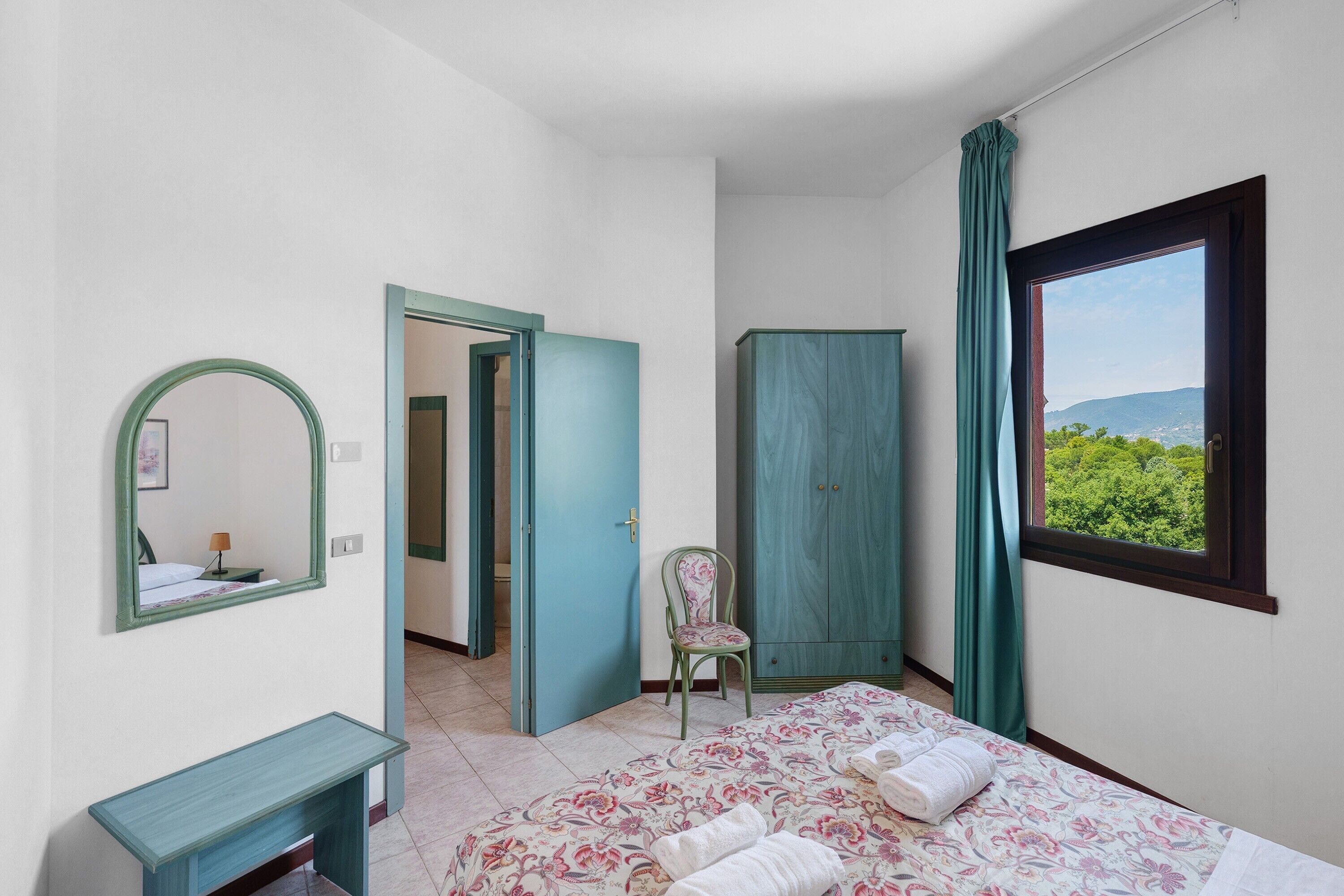 Een slaapkamer met een bed, een stoel, een kledingkast, een spiegel en een raam met uitzicht.