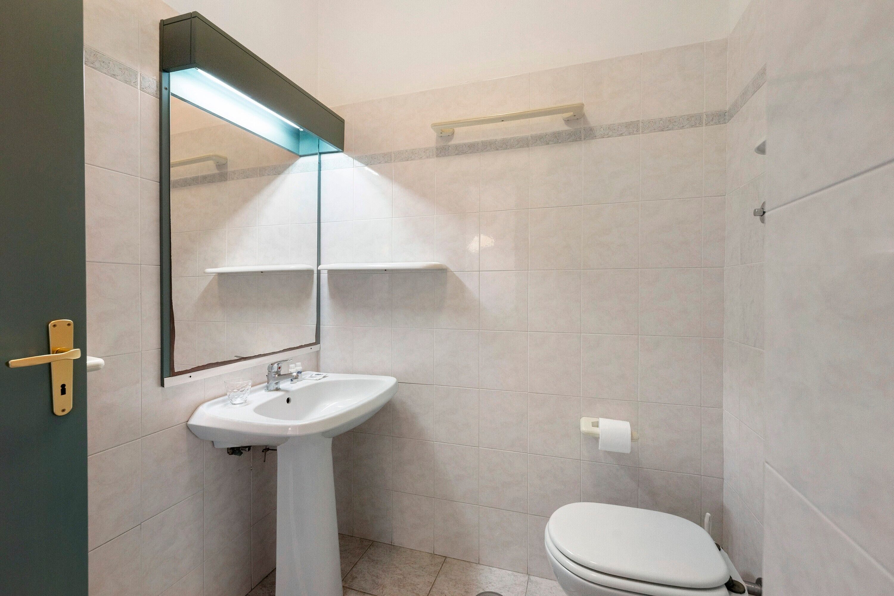 Un bagno con lavandino bianco, specchio e water.