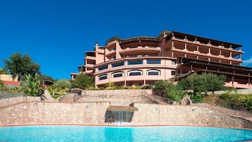 Een hotel met meerdere verdiepingen, een zwembad, stenen muren en een helderblauwe lucht.