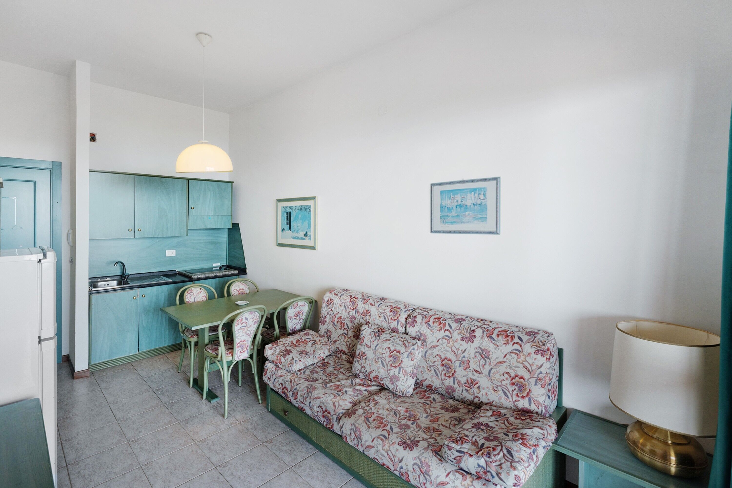 A compact living space with a kitchenette, a sofa, a dining table with chairs, and a lamp.