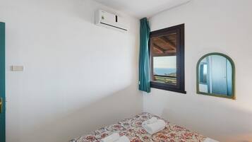 Un lit simple avec une literie à motifs floraux, un appareil de climatisation, une fenêtre avec vue et un miroir au mur.