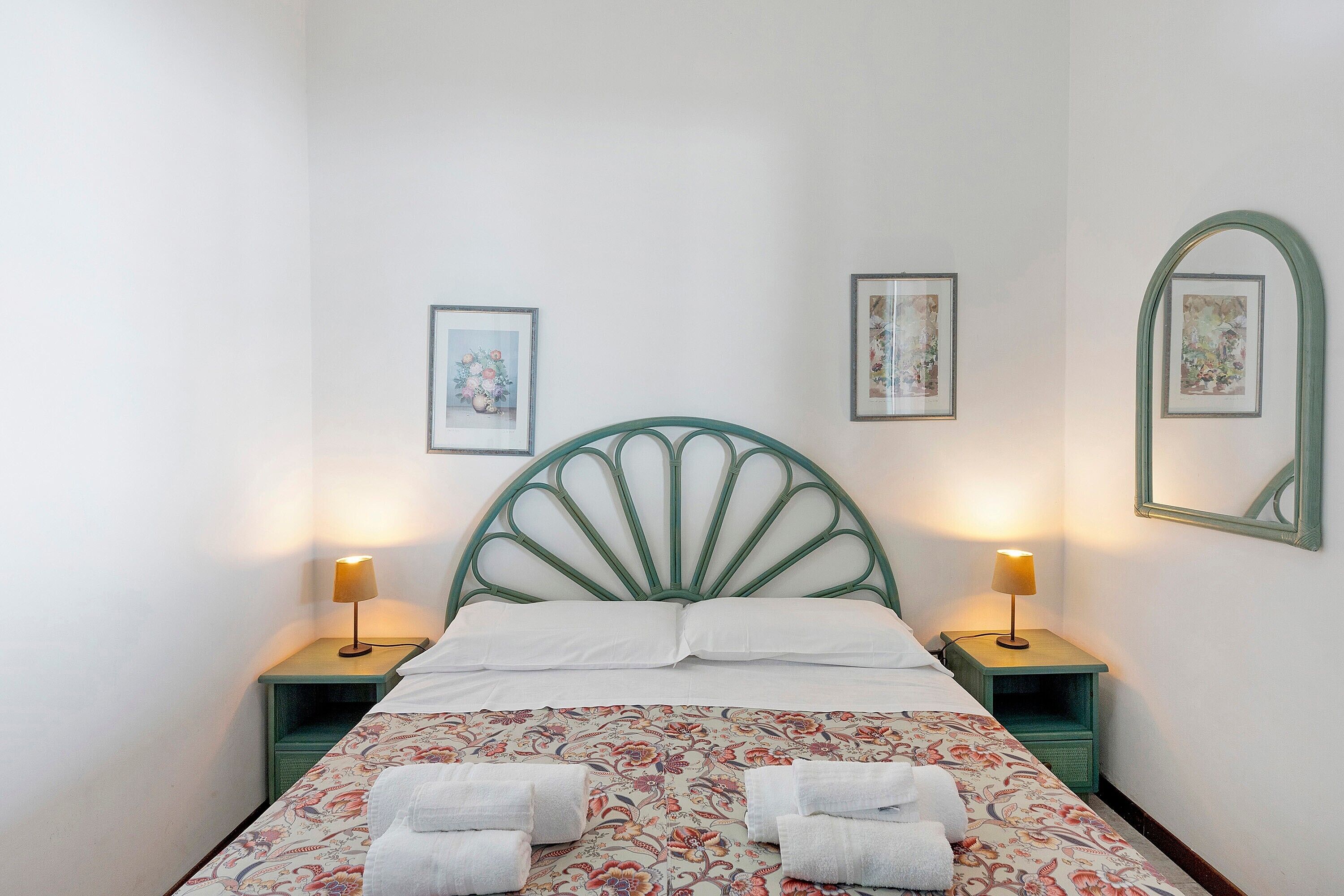 A bed with a green headboard, two bedside tables with lamps, and two framed pictures on the wall.