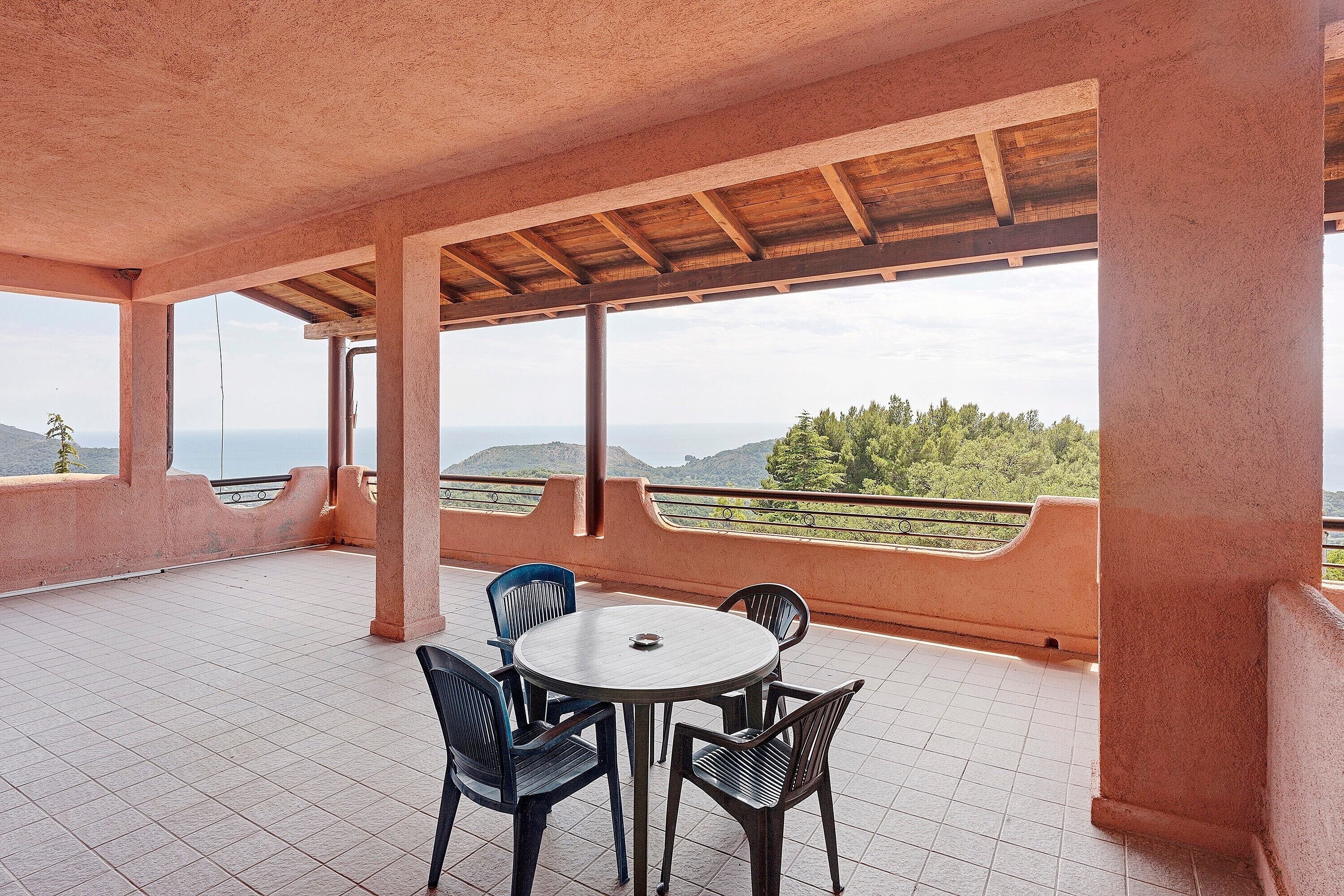 A covered terrace with a round table and chairs, a view of the landscape, and a railing.