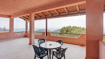 A covered terrace with a round table and chairs, a view of the landscape, and a railing.