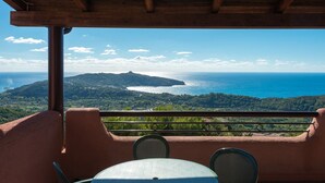 A balcony with a table and chairs, overlooking a coastal landscape with a hill and the sea. - P.R. Club - Three-Room Enea 32 with Sea View, Private Terrace and Air Conditioning (Centola)