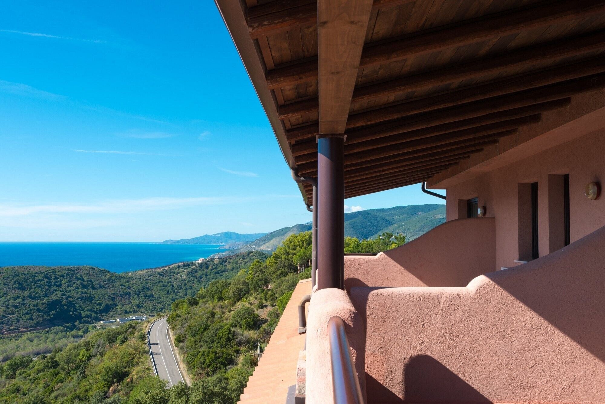 Un balcon offrant une vue sur un paysage côtier, une route et des collines lointaines.