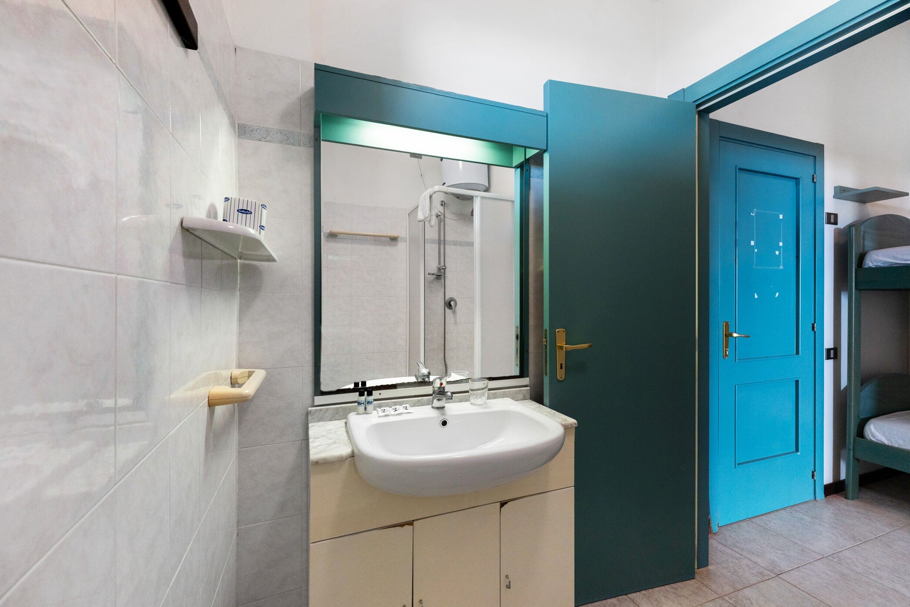 Een badkamer met een wit wastafelmeubel, een spiegel, een douche en een blauwe deur.