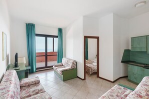 A room with a sofa, a small table with a lamp, a TV, a kitchenette, and a balcony with curtains. - P.R. Club - Three-Room Enea 40 with Sea View, Private Terrace, and Air Conditioning (Centola)