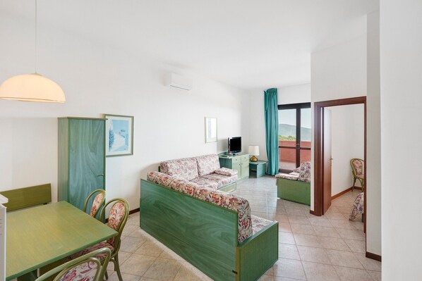 A room with a green sofa, a dining table, chairs, a TV, and a view of the outdoors. - P.R. Club - Three-Room Enea 40 with Sea View, Private Terrace, and Air Conditioning (Centola)