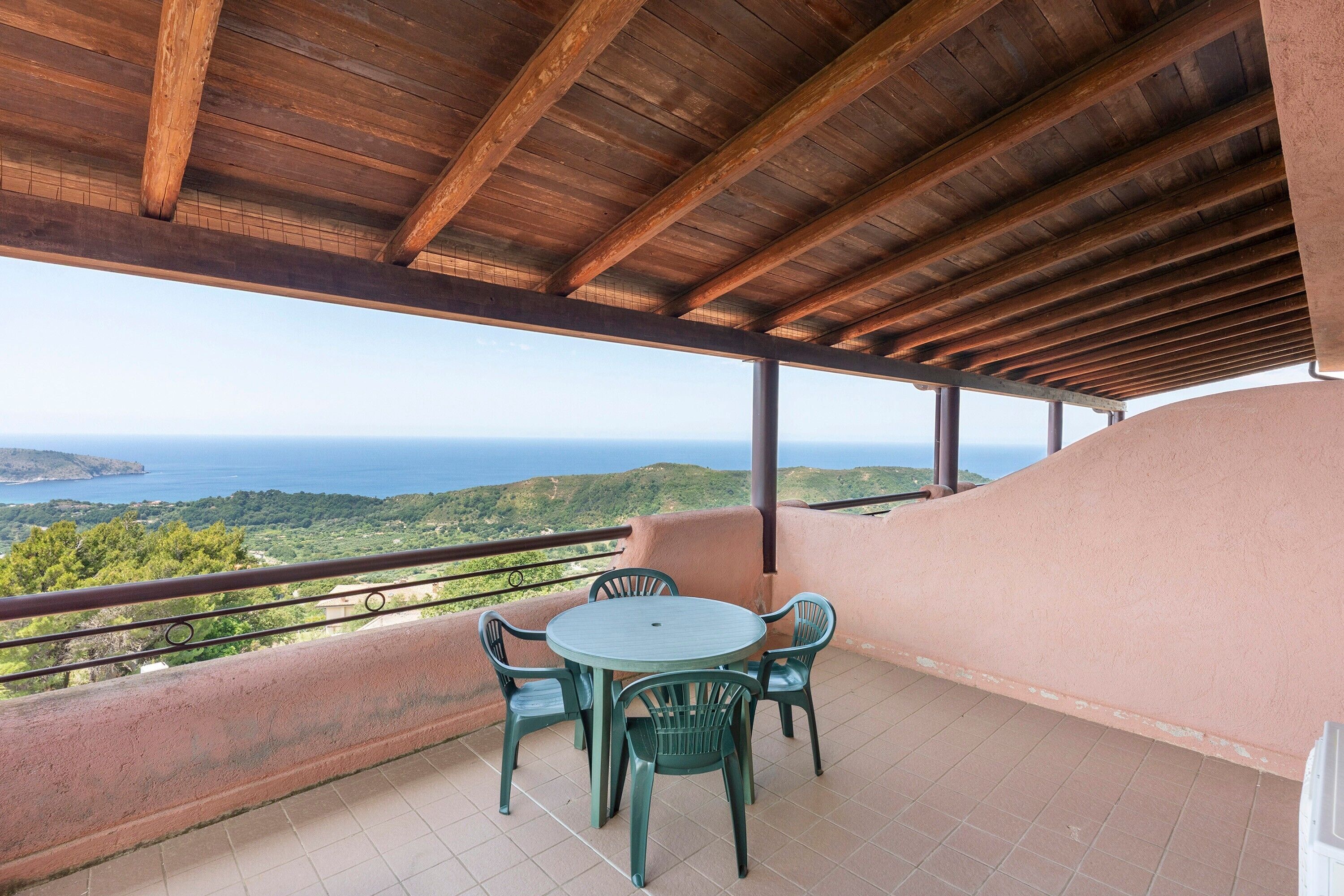 Un espacio al aire libre cubierto con una mesa y sillas, vista al mar y barandilla de balcón.