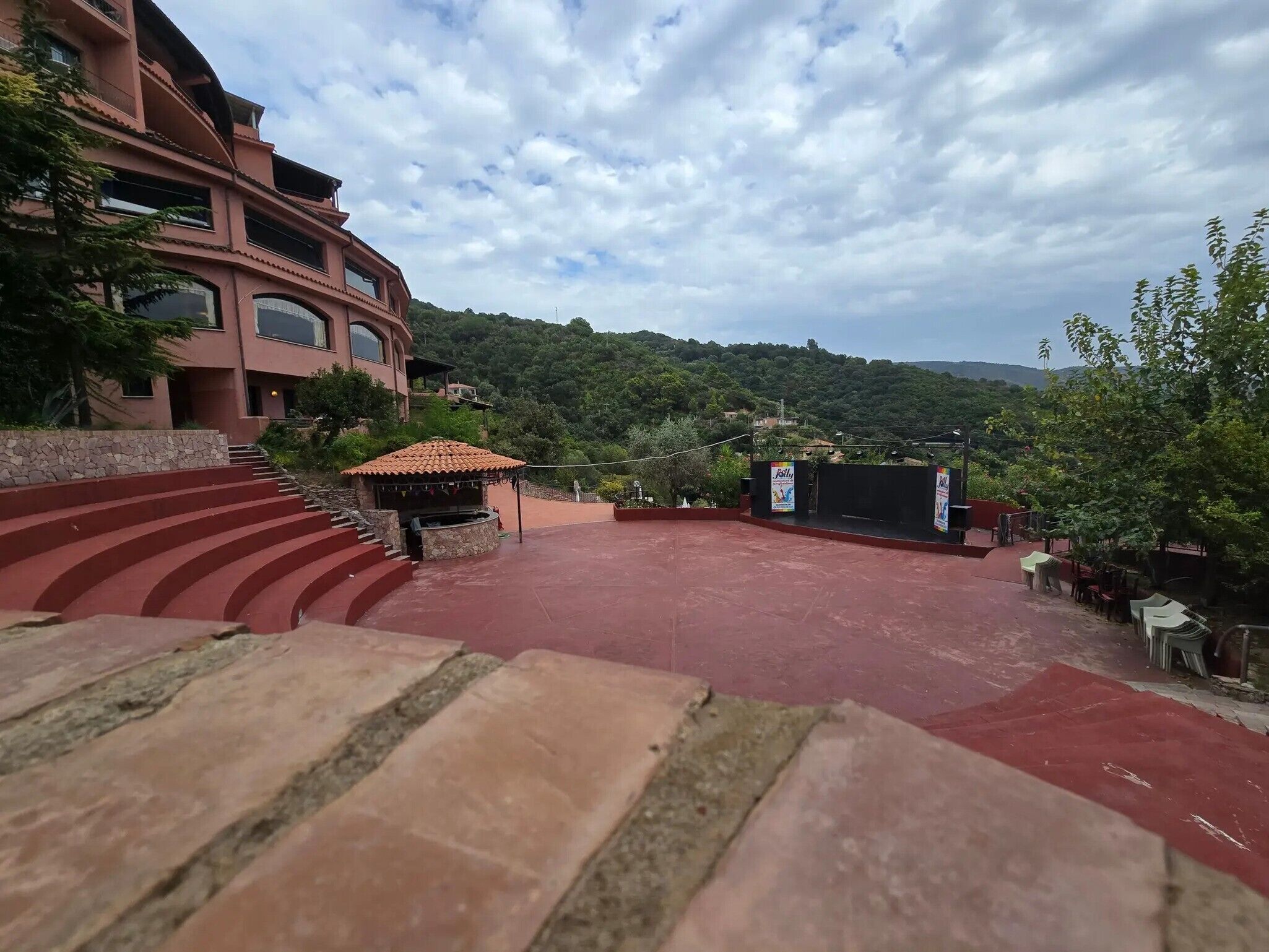 A red carpeted outdoor area with steps leading up to a building, a small kiosk, and a stage with a banner.