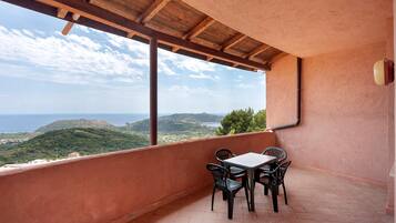 Un balcon avec une table et des chaises, une vue sur la mer et un paysage montagneux.
