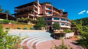 A multi-story hotel with a curved facade, outdoor steps leading to the entrance, and a small gazebo-like structure. - P.R. Club - One-Bedroom Apartment Faro 27 with Sea View, Private Terrace and Air Conditioning (Centola)