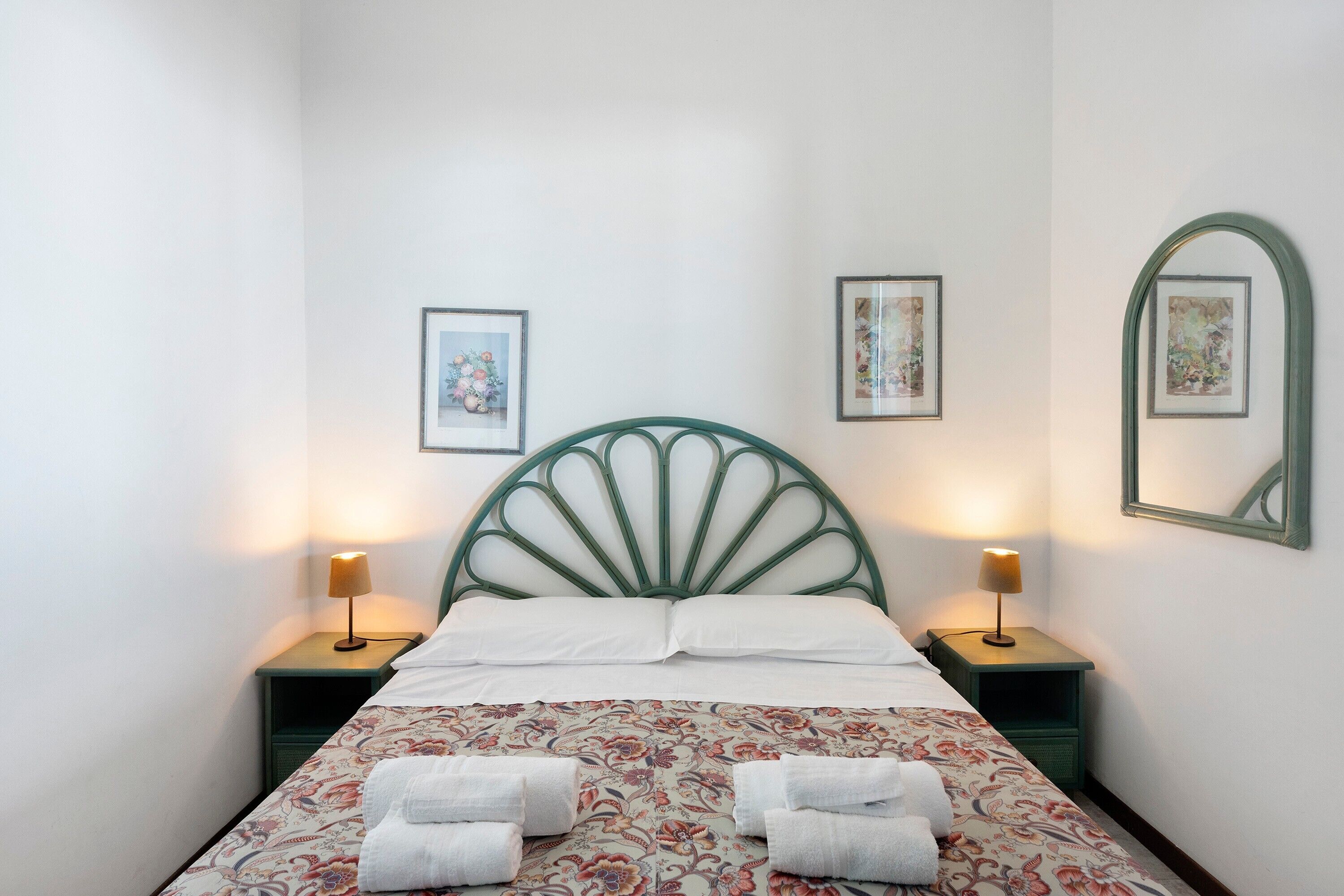 Un lit avec une tête de lit verte, deux tables de chevet avec des lampes et une literie à motifs floraux.