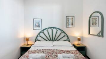 Un lit avec une tête de lit verte, deux tables de chevet avec des lampes et une literie à motifs floraux.