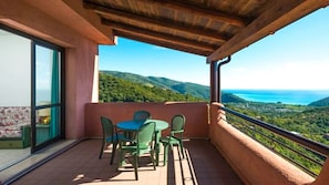 Un balcón con mesa y sillas, con vistas a un paisaje pintoresco con colinas y el mar.