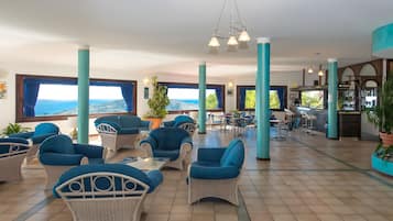 Un espace intérieur vaste et lumineux, aménagé avec des meubles en osier, de grandes fenêtres et offrant une vue sur la mer.