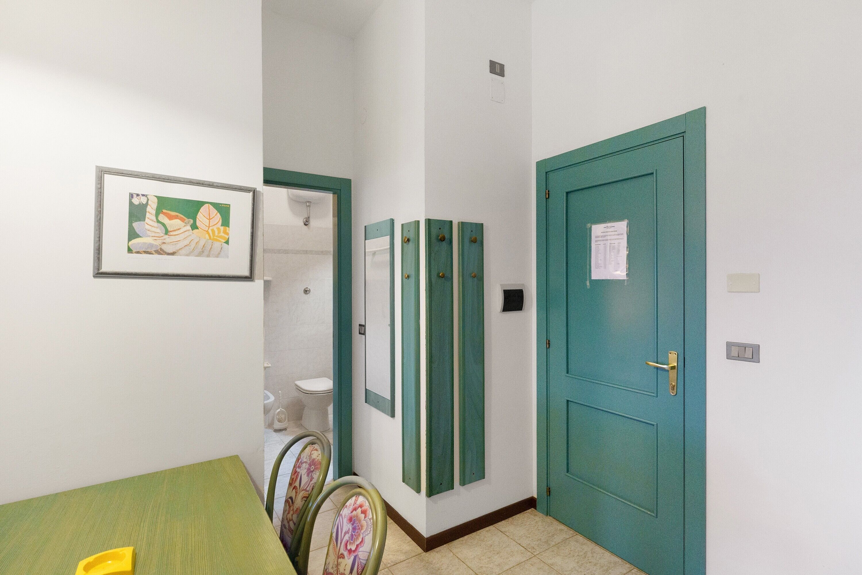 Une pièce avec une table verte, des chaises, un tableau encadré au mur et une porte de couleur turquoise.
