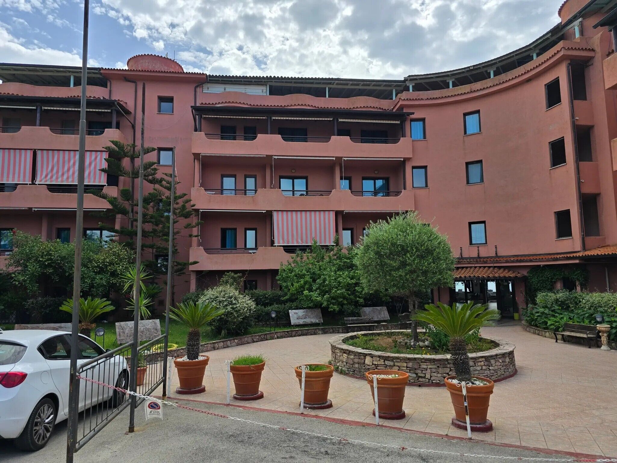 Un edificio de varios pisos con balcones, plantas en macetas y una entrada protegida por una puerta.