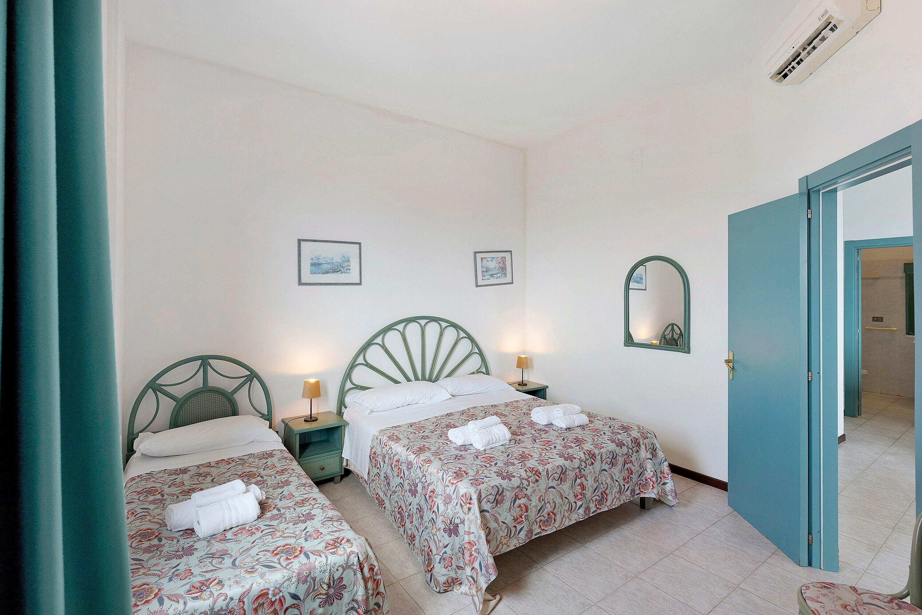 Une chambre d’hôtel avec deux lits simples, une salle de bain visible à travers une porte ouverte et une petite table avec une lampe.