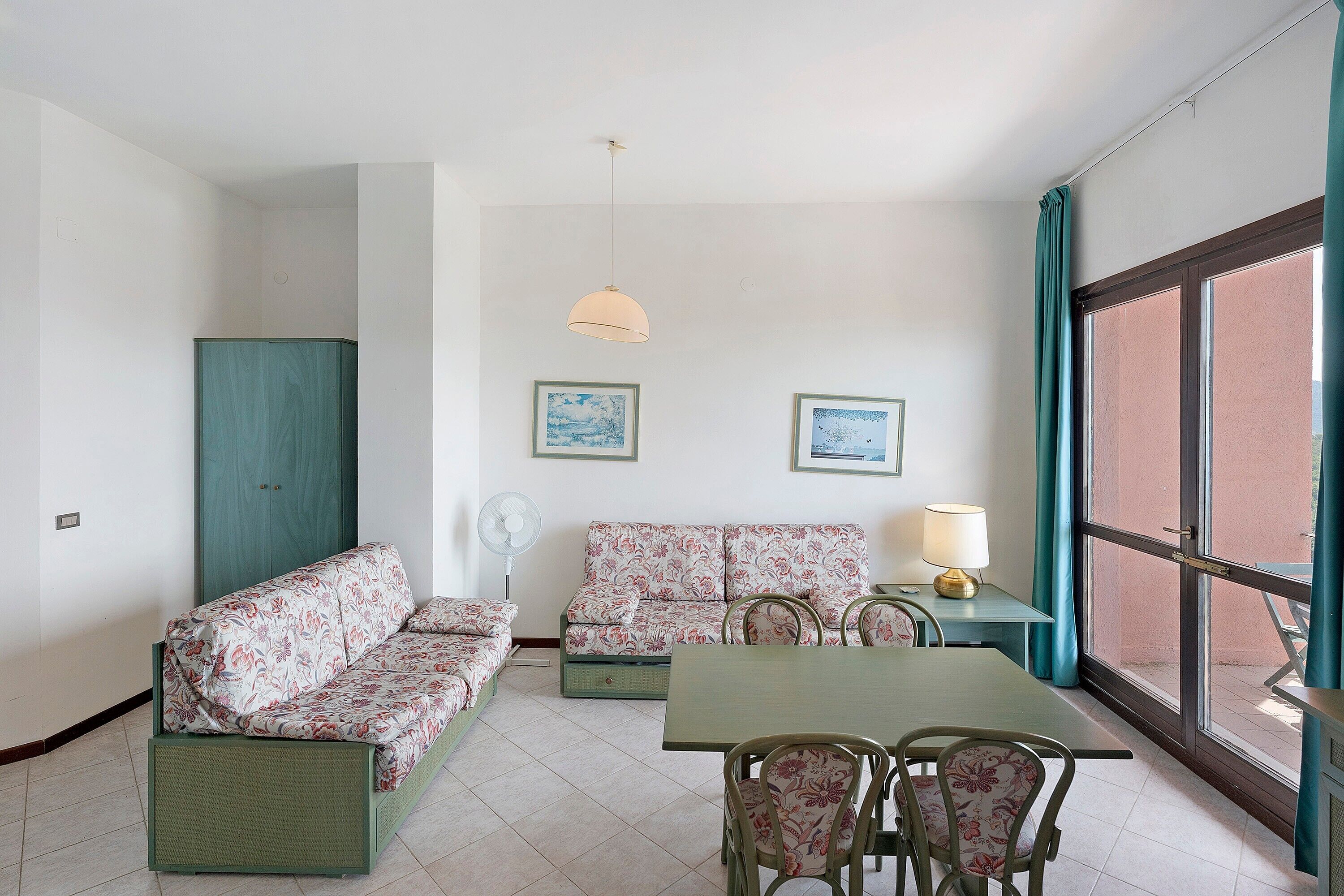 Una habitación con un conjunto de sofá, una mesa con sillas, un ventilador y dos cuadros en la pared.