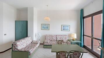 Una habitación con un conjunto de sofá, una mesa con sillas, un ventilador y dos cuadros en la pared.