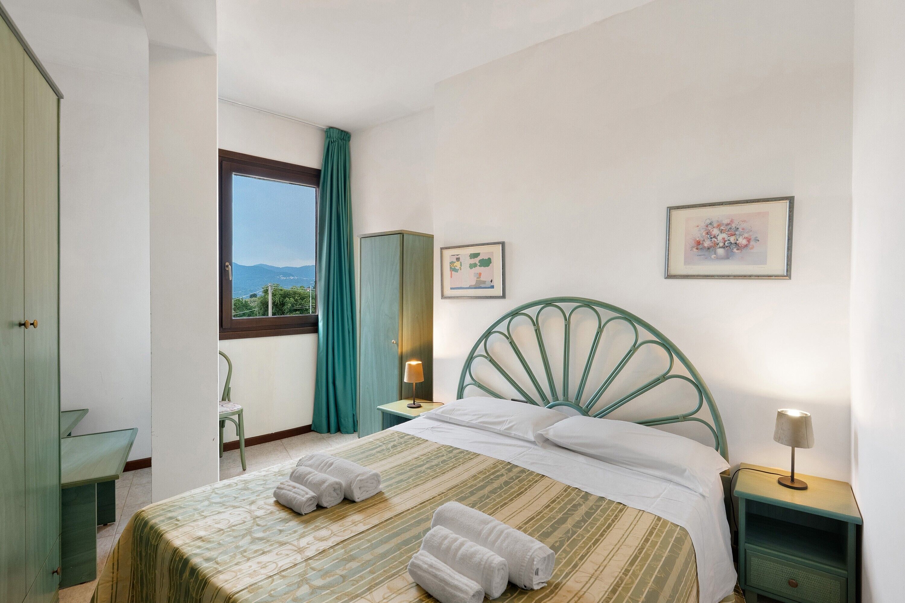 Un dormitorio con cama, mesita de noche, silla, armario y ventana con vistas.