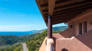 A balcony with a view of a coastal landscape, a road, and distant hills.